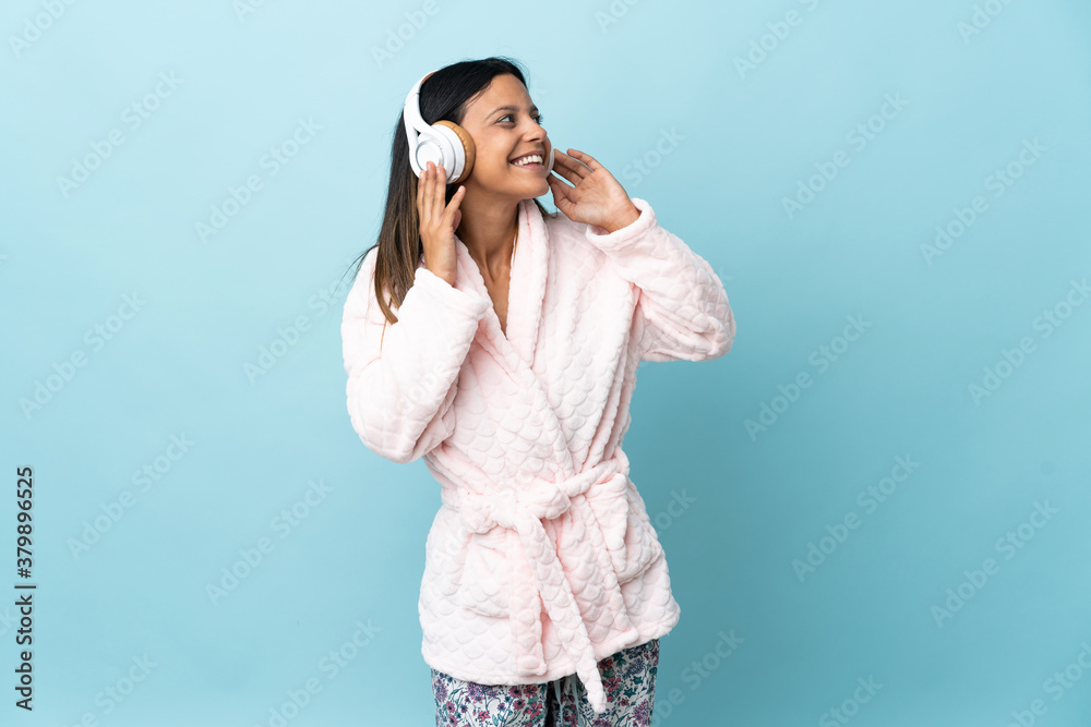 Young woman in pajamas over isolated background in pajamas and holding a pillow and listening music Young woman in pajamas over isolated background in pajamas and holding a pillow and listening music