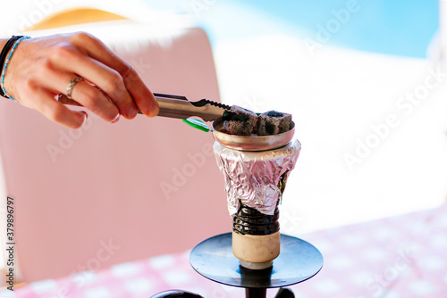 young blonde person preparing and smoking a hookah on a terrace in summer