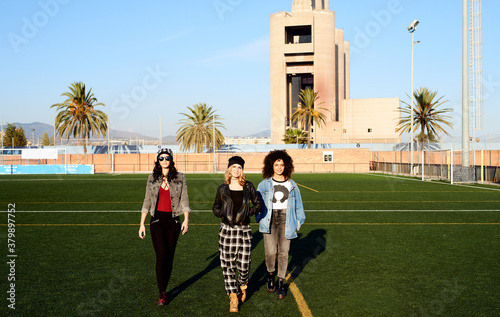 Smiling teen girls walking towards camera on pitch.