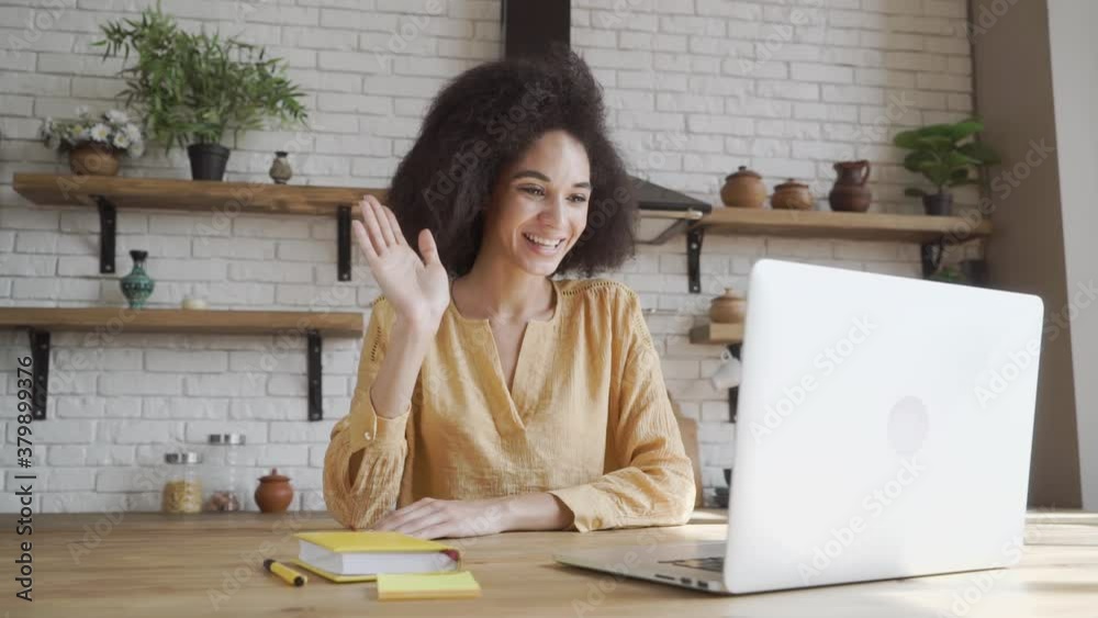 Happy african american young woman looking at computer screen, waving hello. Pleasant attractive mixed race female professional holding video call with client. Happy african american young woman looking at computer screen, waving hello. Pleasant attractive mixed race female professional holding video call with client.