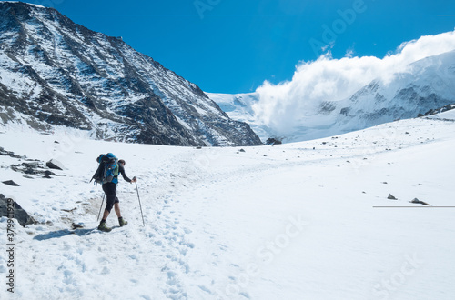 Active climber backpacker man with trekking poles and backpack climbing Mont Blank mount in French Alps mountains during high altitude acclimatization walking. Extreme active people concept image.