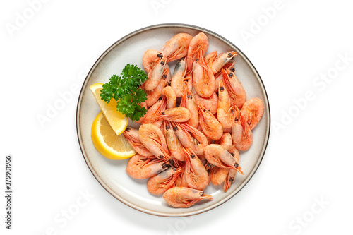 Boiled shrimp prawns in a shell with lemon and parsley in a plate on a white background. Top view