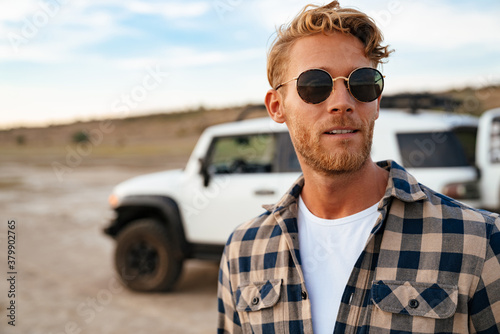 Confident young man walking at the beach with his car