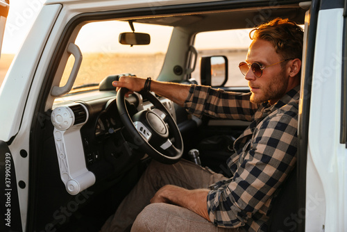 Attractive young man sitting on a front sit in hos car at the beach, open door photo