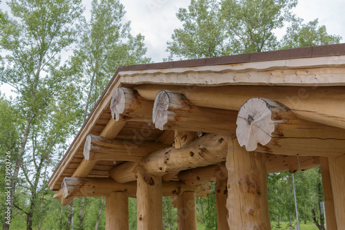 A large shed with a roof made of huge wooden logs. Construction concept without nails. Background - green forest.
