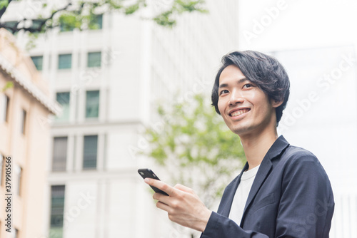 オフィス街でスマートフォンを操作する若い男性