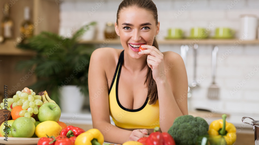 Sporty woman biting cherry tomato at home kitchen Sporty woman biting cherry tomato at home kitchen