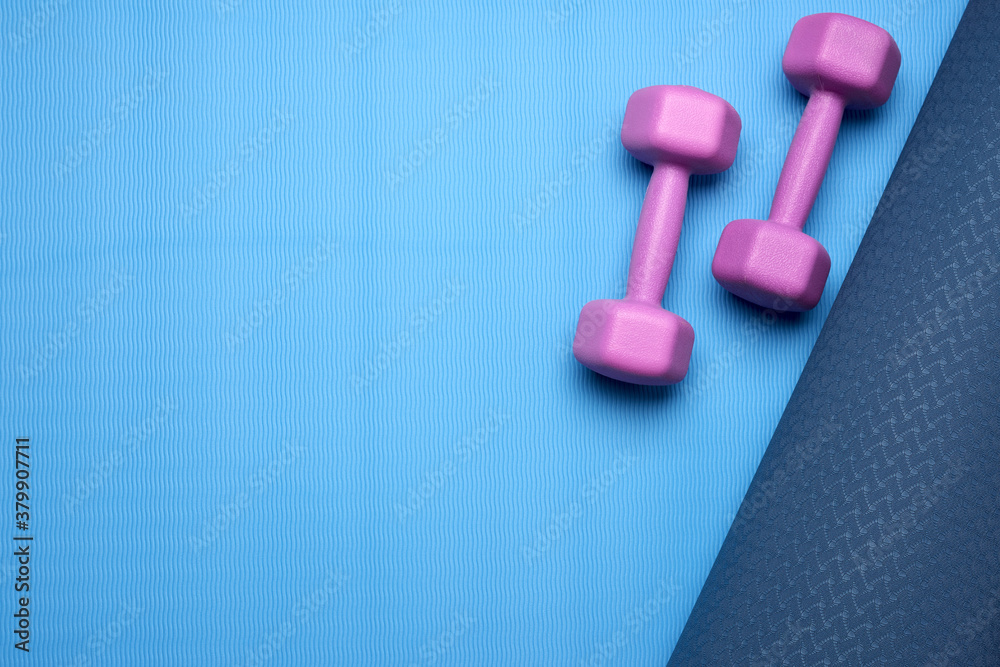 pair of purple dumbbells on a blue neoprene mat, top view pair of purple dumbbells on a blue neoprene mat, top view