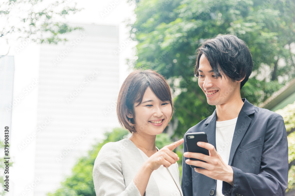オフィス街でスマートフォンを見ながら会話する男女 オフィス街でスマートフォンを見ながら会話する男女