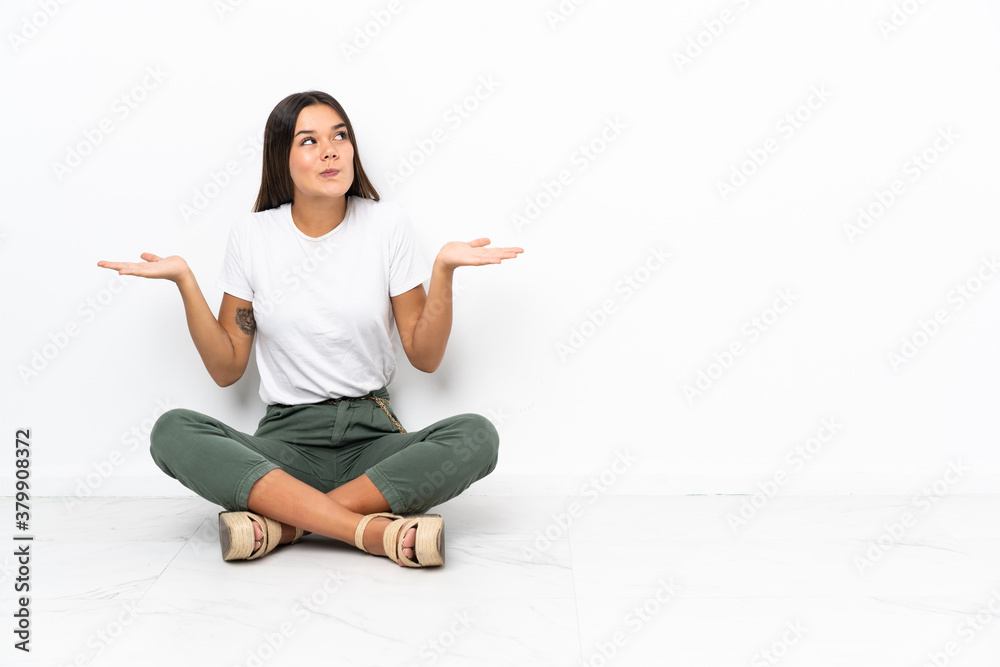 Teenager girl sitting on the floor having doubts while raising hands Teenager girl sitting on the floor having doubts while raising hands