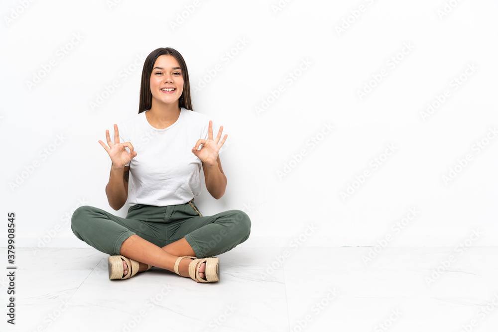 Teenager girl sitting on the floor showing an ok sign with fingers