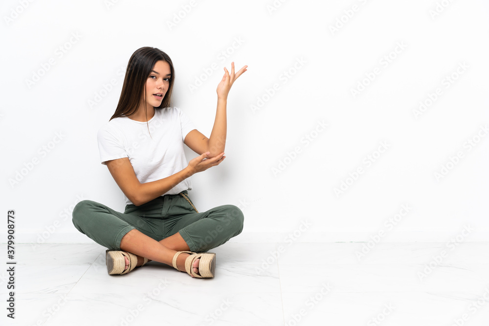 Teenager girl sitting on the floor extending hands to the side for inviting to come Teenager girl sitting on the floor extending hands to the side for inviting to come