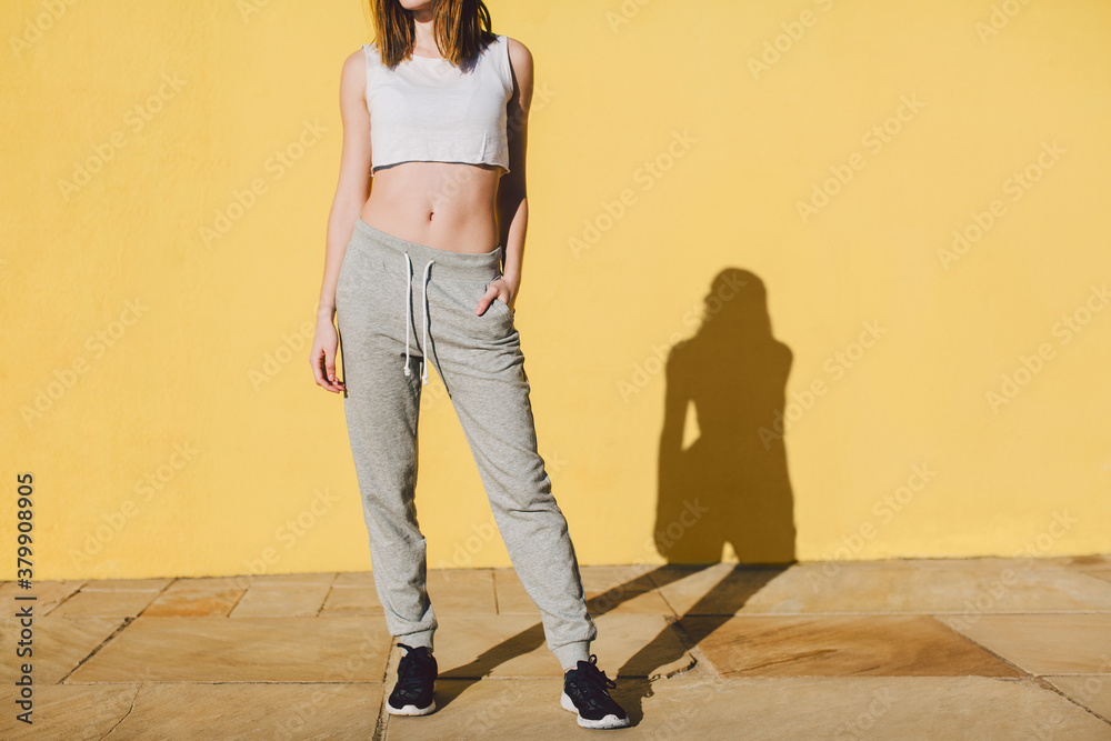 Fit woman wearing sport clothes standing in front of a yellow wall. Fit woman wearing sport clothes standing in front of a yellow wall.