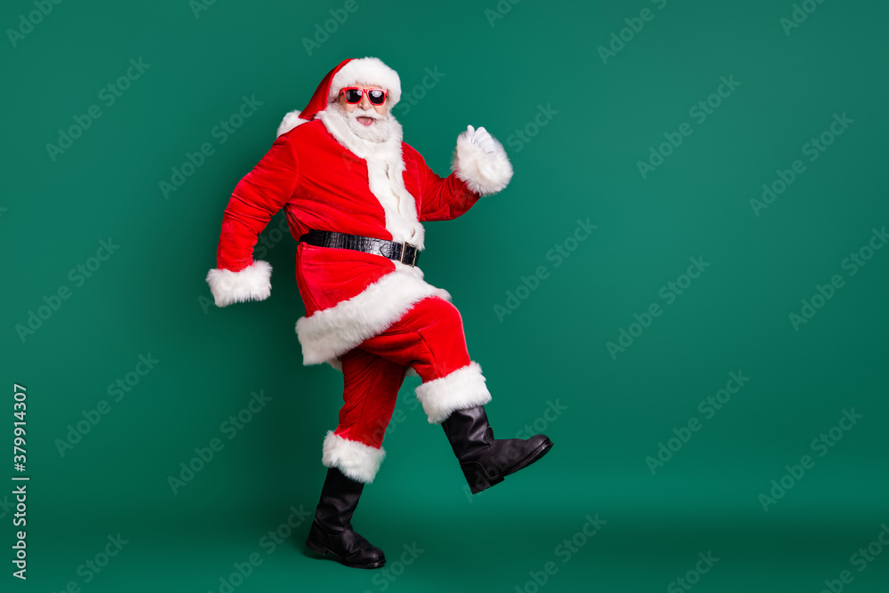 Full body size profile photo of retired grandpa funny walk together elves deer buy present gift kids wear red santa costume coat gloves sunglass cap isolated green color background Full body size profile photo of retired grandpa funny walk together elves deer buy present gift kids wear red santa costume coat gloves sunglass cap isolated green color background