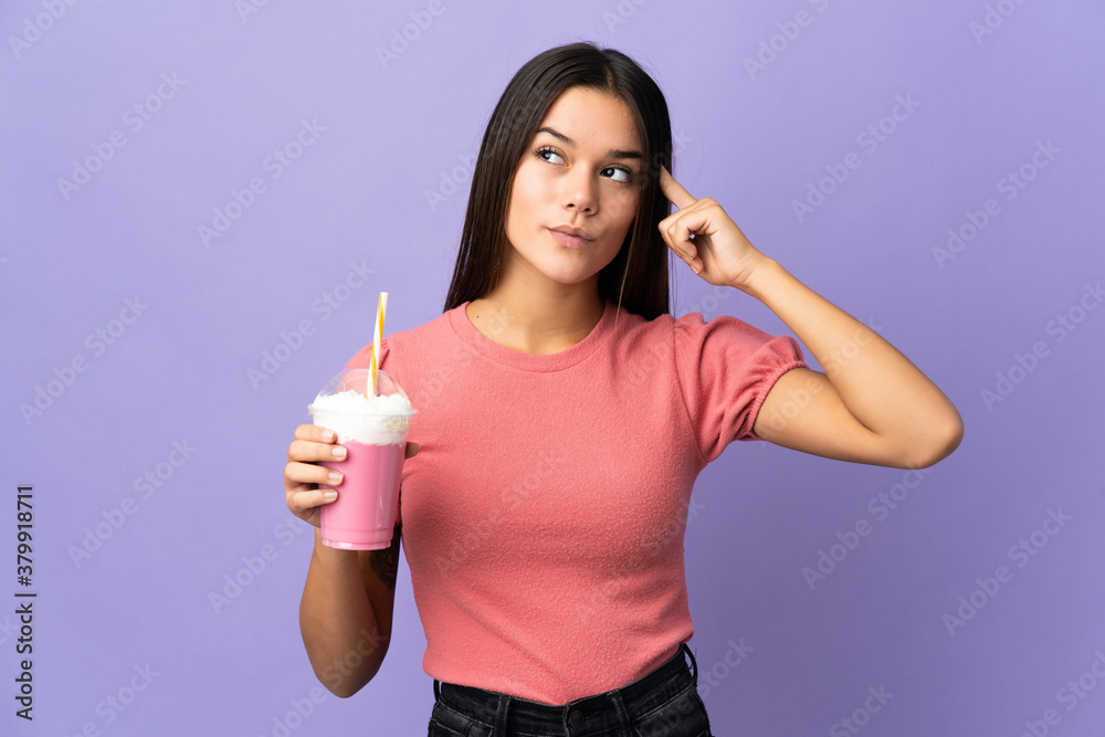 Teenager girl holding a strawberry milkshake having doubts and thinking Teenager girl holding a strawberry milkshake having doubts and thinking