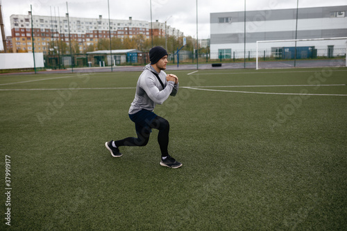 Side view of an active young man in sportswear performing lunges during a functional workout