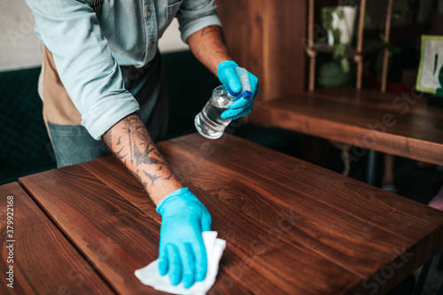 Handsome middle age waiter cleaning and disinfecting restaurant table for next customer. Corona virus and small business is open for work concept.