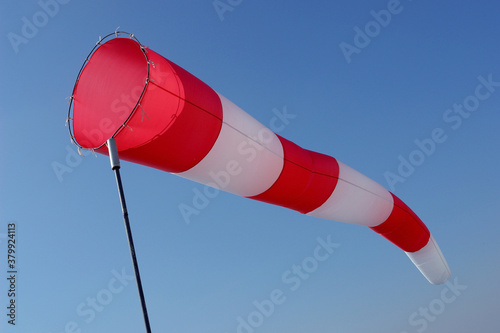 Red and white windsock against the blue sky. Concept of wind, climate, weather forecast.