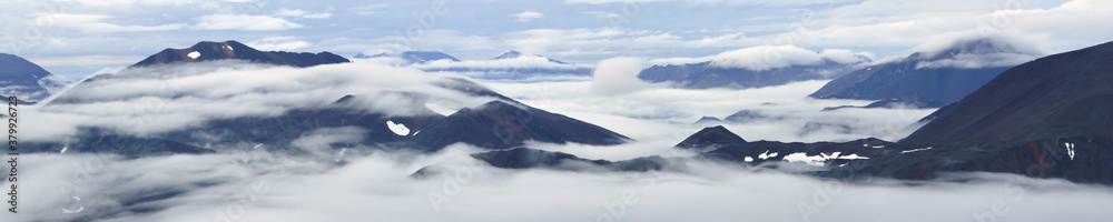 Majestic mountain panorama. Mountain tops among clouds and fog. Harsh Arctic landscape. Travel, Hiking and mountain climbing in the far North of Russia. Northern nature of Chukotka and Polar Siberia.