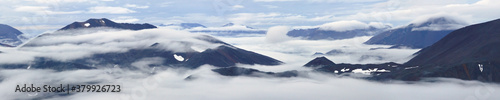 Majestic mountain panorama. Mountain tops among clouds and fog. Harsh Arctic landscape. Travel, Hiking and mountain climbing in the far North of Russia. Northern nature of Chukotka and Polar Siberia.