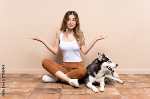 Young pretty woman with her husky dog sitting in the floor at indoors with shocked facial expression