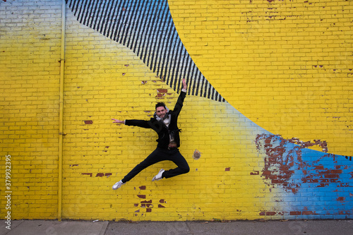 danseur en plein saut devant un mur de brique recouvert d'un immense graffiti en milieu urbain 