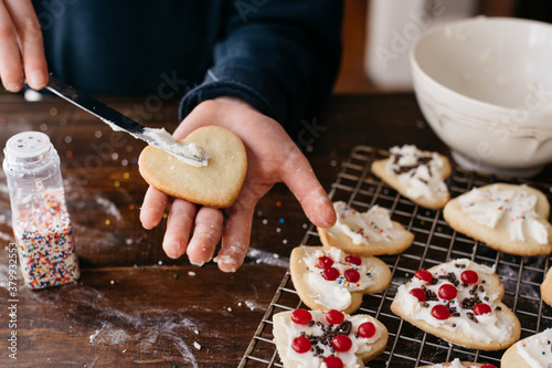 Hand of a girl spreading frosting on a heart shaped cookie