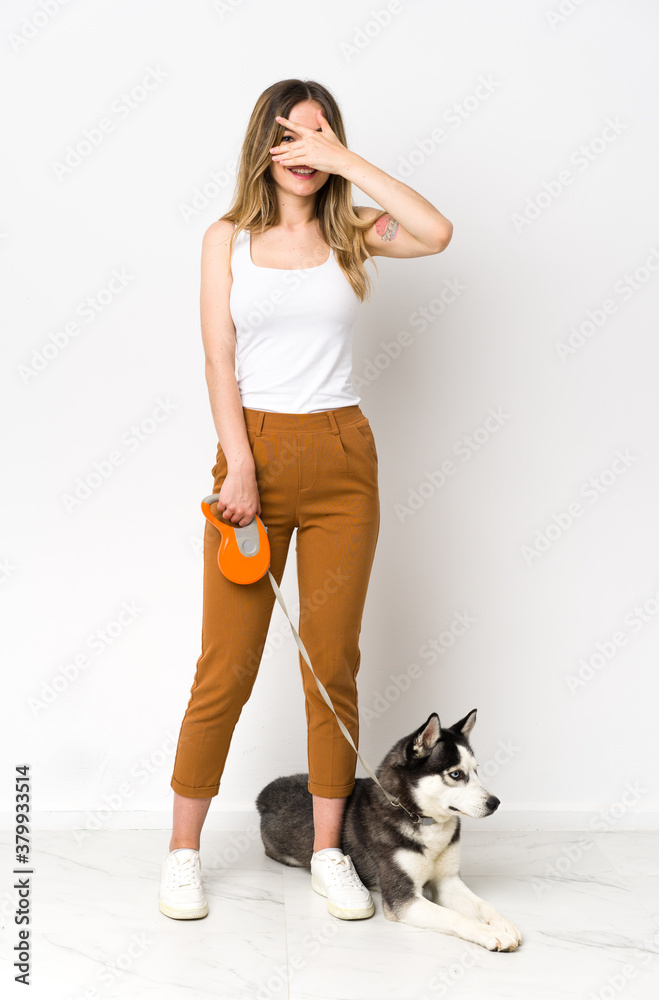 A full length young pretty woman with her dog covering eyes by hands and smiling