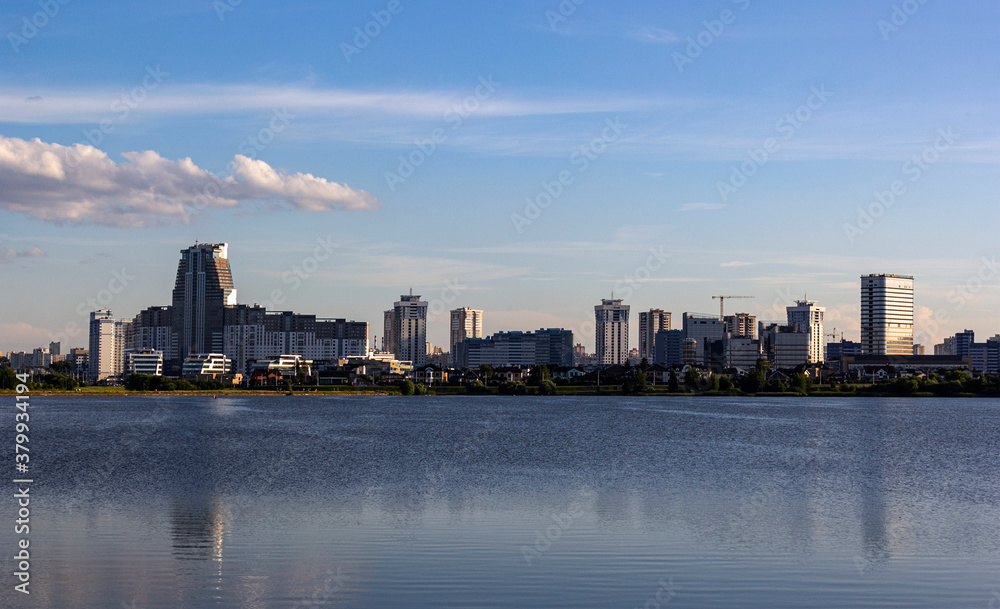Obraz premium Panorama of the skyline of Minsk through Lake Drozdy in the daytime. Water smoothness with reflection