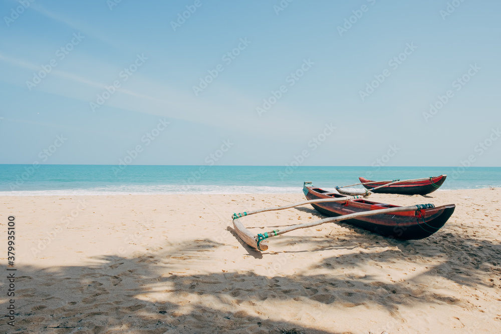 Fishing boats in a quiet beach with palm trees shadow