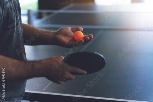 A young man is playing ping pong. He holds a ball and a racket in his hands photo