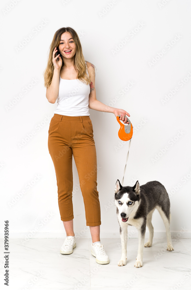 A full length young pretty woman with her dog keeping a conversation with the mobile phone with someone