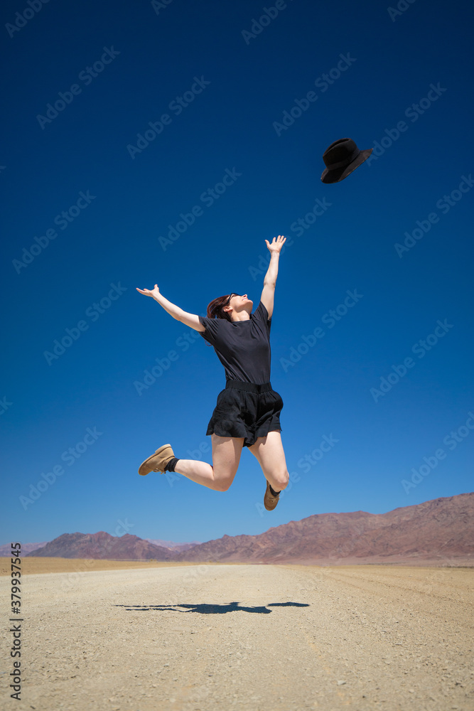 Woman dressed in black jumping for joy in the desert throwing he Woman dressed in black jumping for joy in the desert throwing he