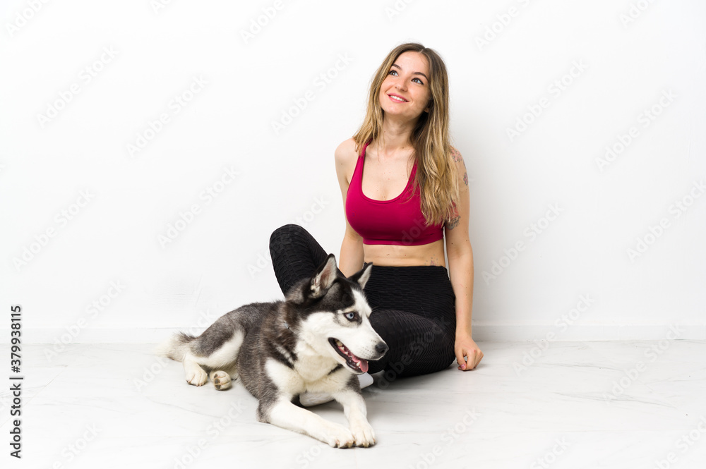 Young sport girl with her dog sitting on the floor looking up while smiling