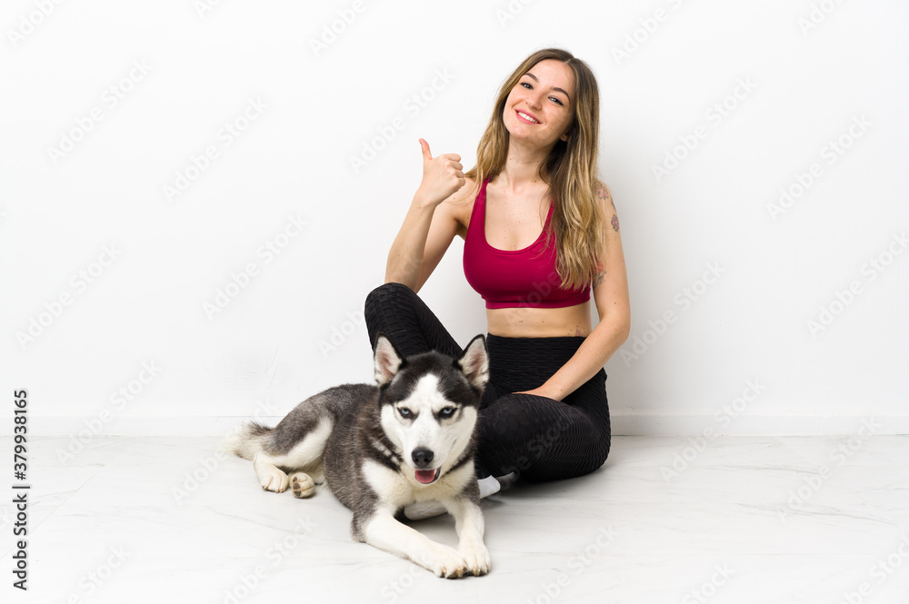 Young sport girl with her dog sitting on the floor with thumbs up because something good has happened
