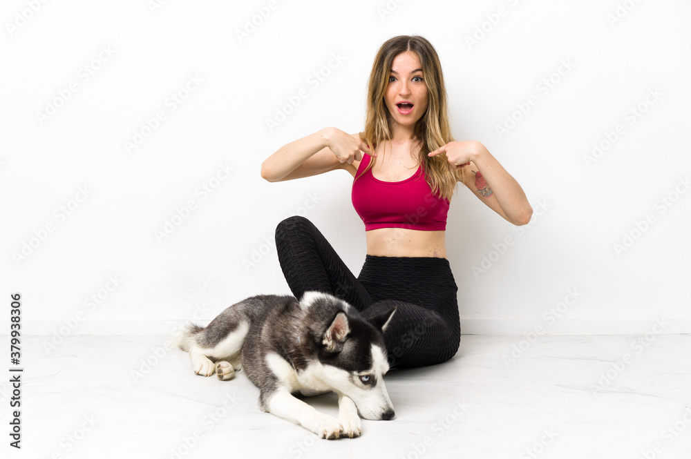 Young sport girl with her dog sitting on the floor with surprise facial expression