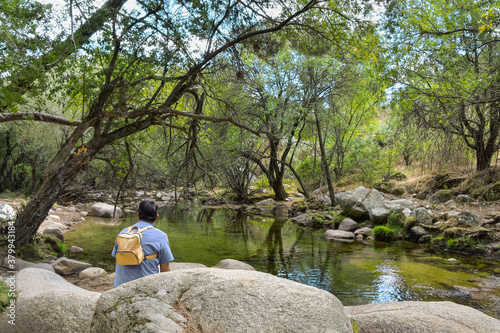 A hiker rests by the backwater of a mountain stream enjoying the peaceful scenery. "Sierra de Guadarrama" National Park, Madrid, Spain