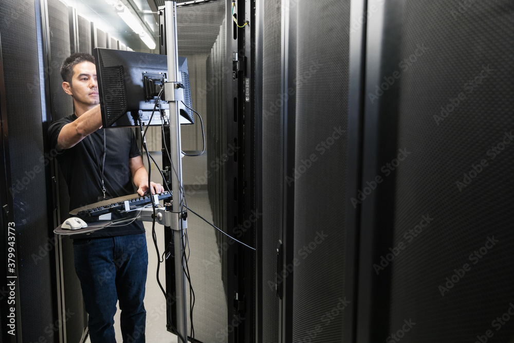 Technician stands at a computer station in a server room Technician stands at a computer station in a server room