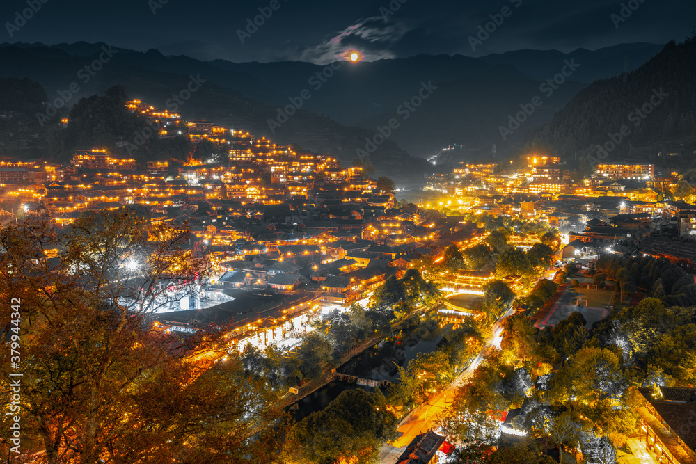 Fototapeta premium GUIZHOU, CHINA - APRIL 17: Xijiang miao village, largest village in Guizhou Miao ethnic minority, April 17, 2010. Night illumination of houses and bridge over river village in Xijiang. Leishan County.