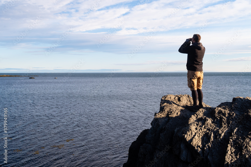 Man standing on a cliff and looking through binoculars in the Bic national park, Canada