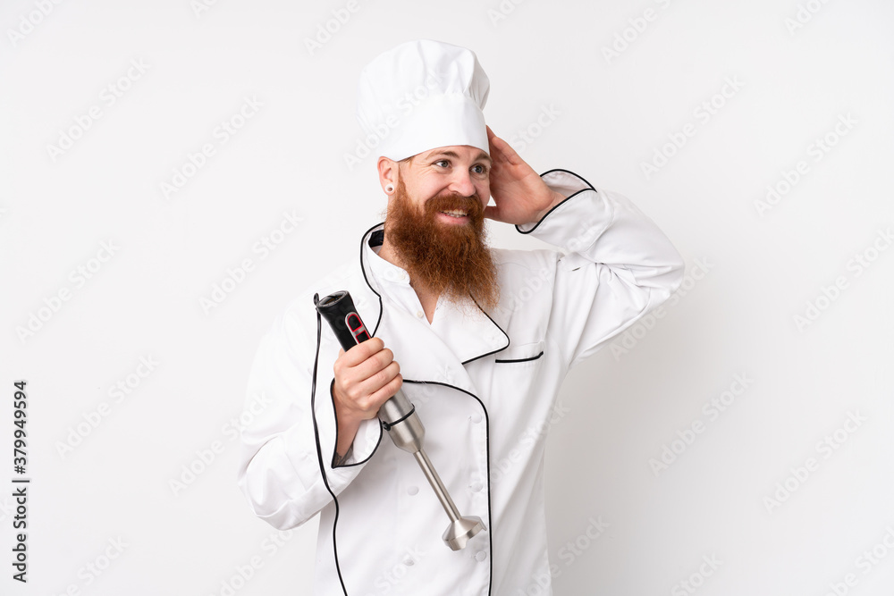 Redhead man using hand blender over isolated white background laughing Redhead man using hand blender over isolated white background laughing
