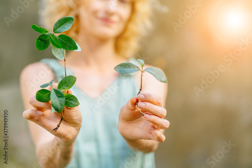 Blond woman housefive holding two sprouts outdoor. Gardening, hobby, leisure concept.