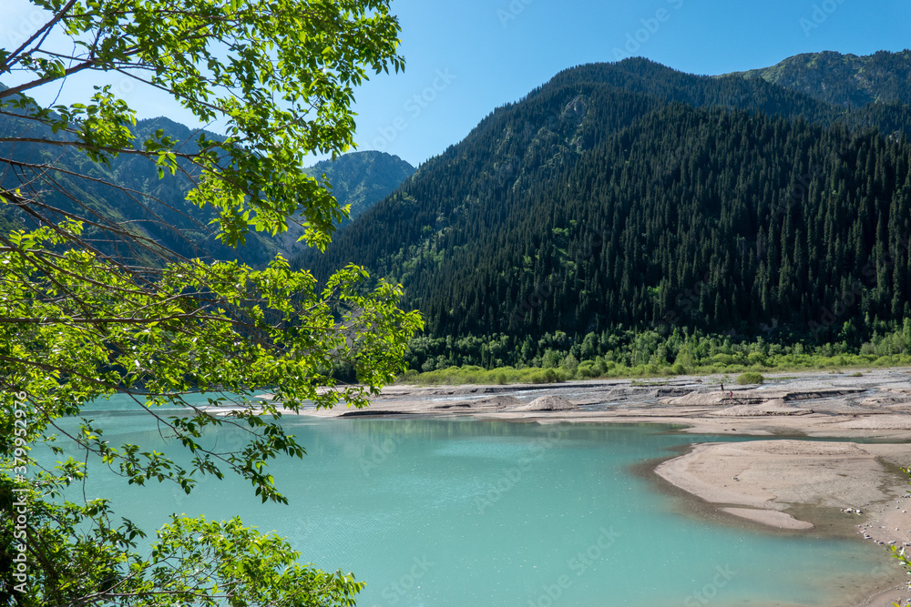 Sandy shore of a bright blue Issyk mountain lake, green forests, mountains. Kazakhstan