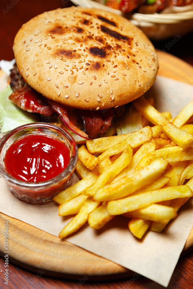 Big fat burger with bacon stripes served on wooden plate on table in  American fast food