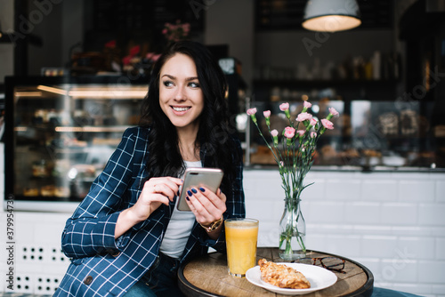 Optimistic woman messaging on smartphone during breakfast in cafe