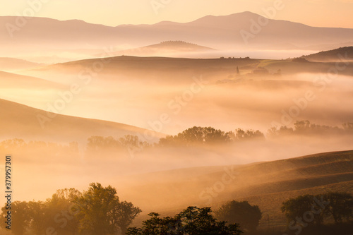 great hill covered by colorful fog, perfect morning in tuscany, italy