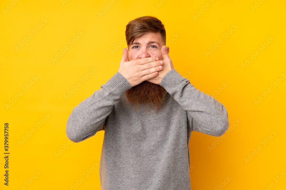 Redhead man with long beard over isolated yellow background covering mouth with hands Redhead man with long beard over isolated yellow background covering mouth with hands