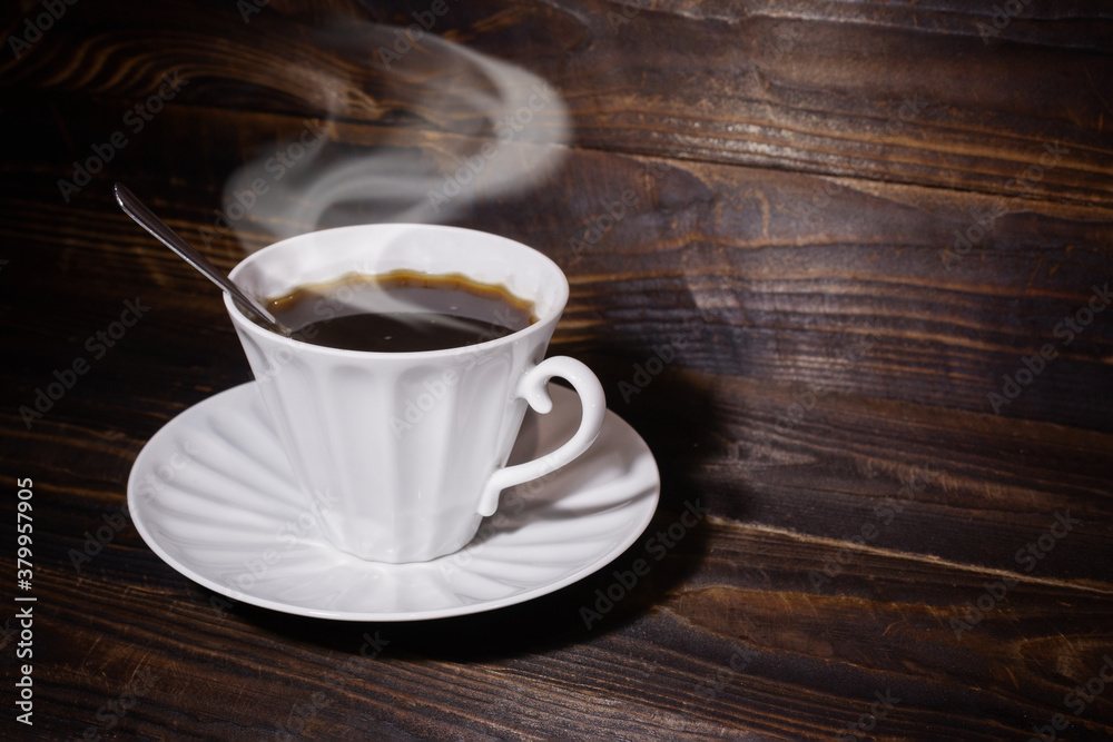 White cup and saucer with coffee and spoon on brown wooden surface, steam over the cup. White cup and saucer with coffee and spoon on brown wooden surface, steam over the cup.