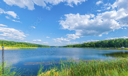 Large lake with blue water in the middle of a forest with green trees on a sunny day. Lake Chaika, Andrushivka, Zhytomyr region, Ukraine