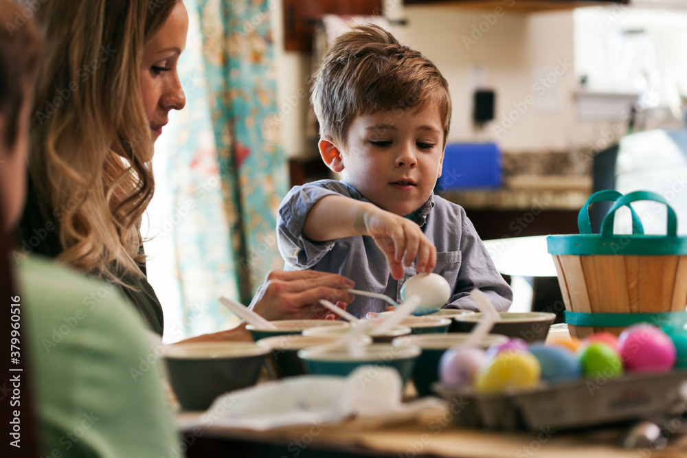 Easter: Boy Carefully Puts Egg Into Blue Dye Easter: Boy Carefully Puts Egg Into Blue Dye